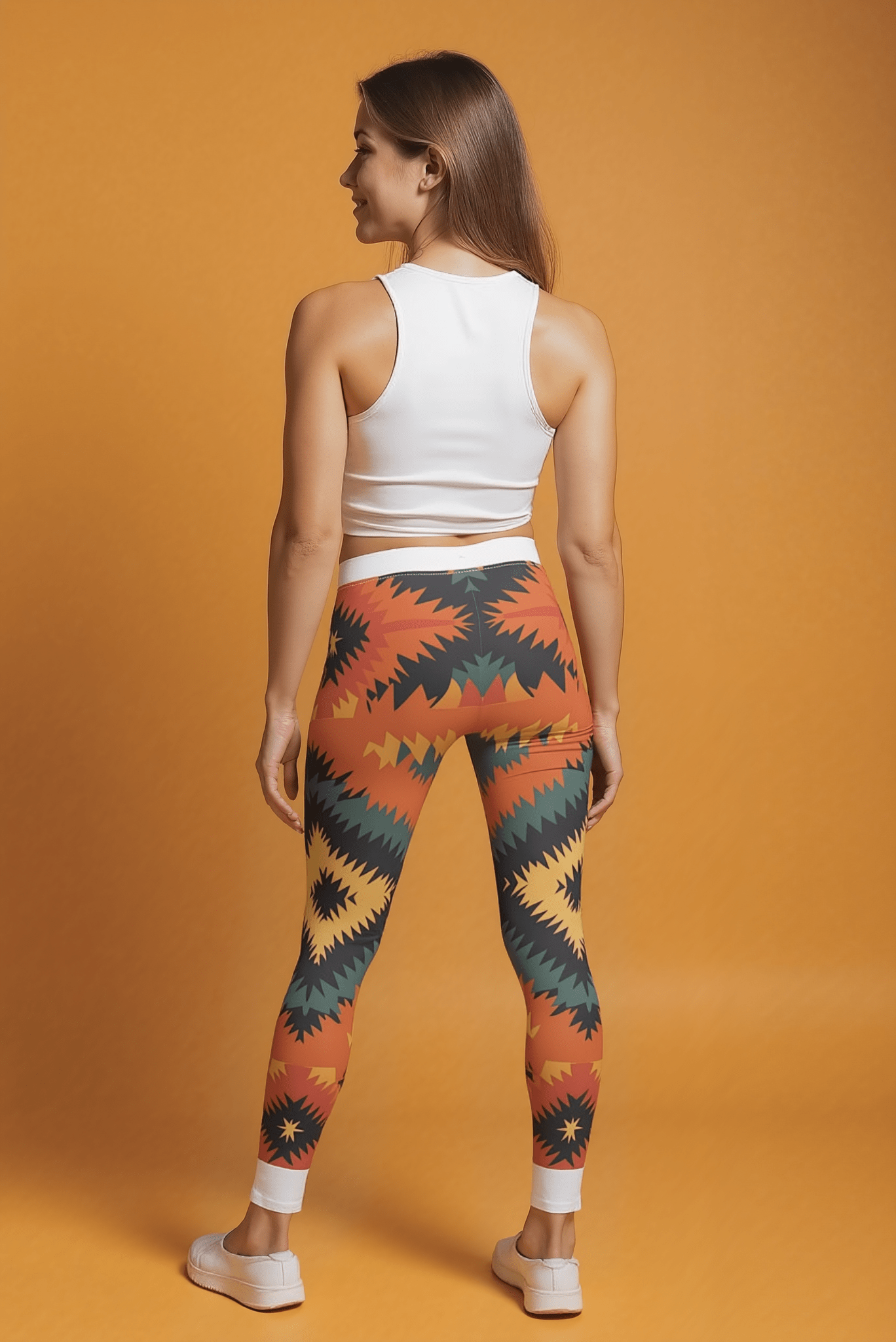 Frau von hinten mit einzigartigen, bedruckten Designer-Leggings in Herbstfarben und weißem Top vor orangem Hintergrund.