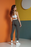 Back view of a fashionable woman in Women's Cut & Sew Casual Leggings (AOP) by Printify, featuring a sleek silhouette and white highlights, smiling while posed in front of a vibrant backdrop.