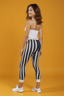 Back view of a model in Casual Striped Leggings, with a playful smile, highlighting the unique design and fit against a striking yellow background.