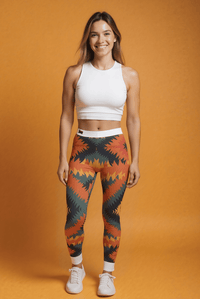 Frau trägt einzigartige Designer-Leggings mit orange-schwarzem Muster, weißes Top, nachhaltige Yoga- und Sportleggings mit hohem Bund.
